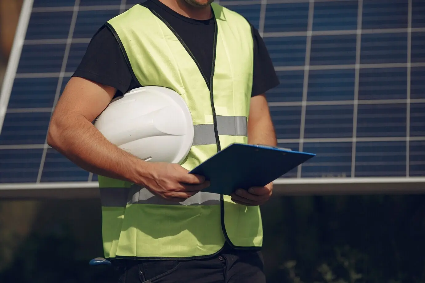A man with a white helmet beside a solar panel.